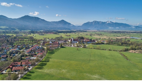 Luftaufnahme des Klosters Benedikbeuern am Ortsrand vor Bergpanorama 