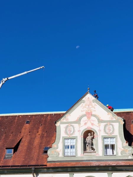 Mittels eines Krans wird eine Plane über die vom Unwetter am 26. August 2023 stark beschädigten Dächer des Klosters Benediktbeuern gezogen